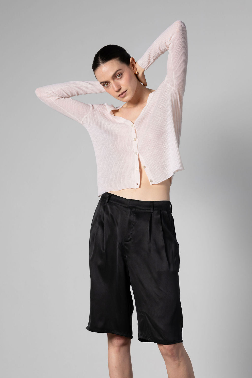 Woman wearing a light pink cashmere cardigan and black shorts on a gray background