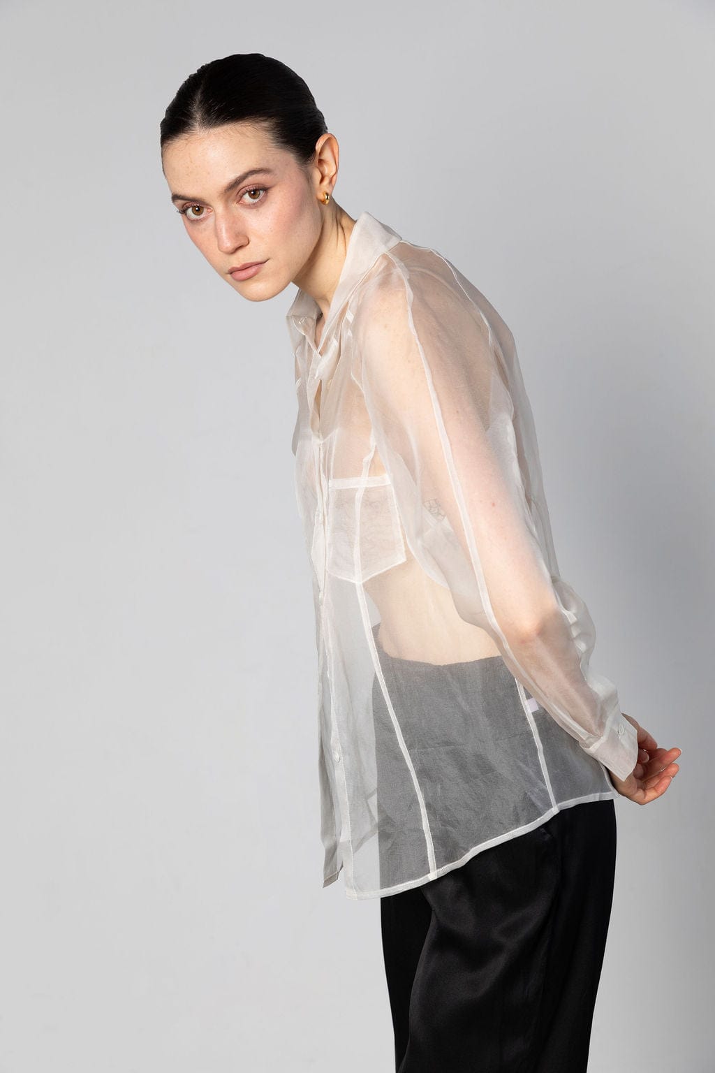 Woman wearing a sheer white blouse over a black outfit on a gray background